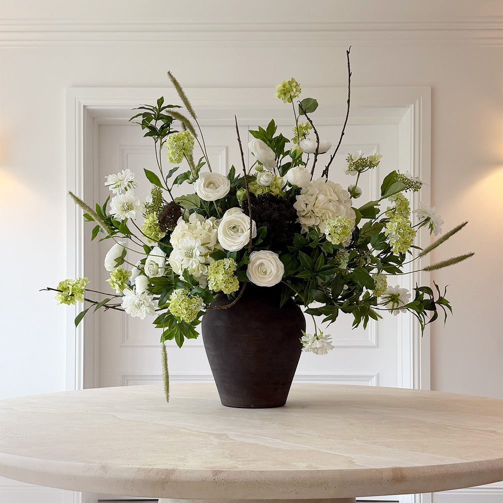 Floral arrangement in a dark vase on a light wooden table with a white wall background