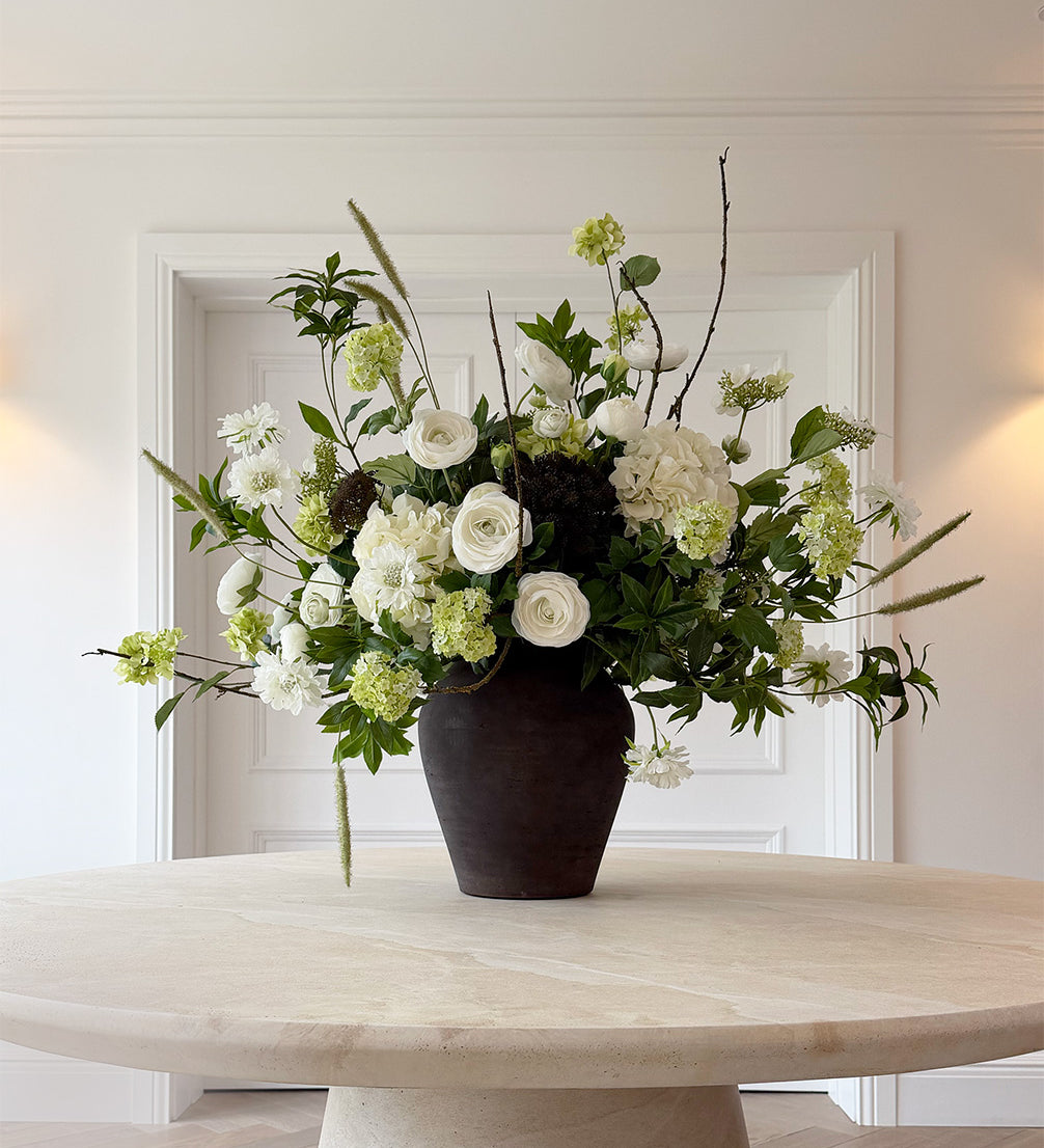 Floral arrangement in a dark vase on a light wooden table with a white wall background
