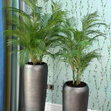 Two tall gray planters with faux green plants against a light blue wall.
