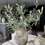 Potted artificial olive tree plant on a wooden table with a blurred indoor background