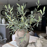 Potted artificial olive tree plant on a wooden table with a blurred indoor background