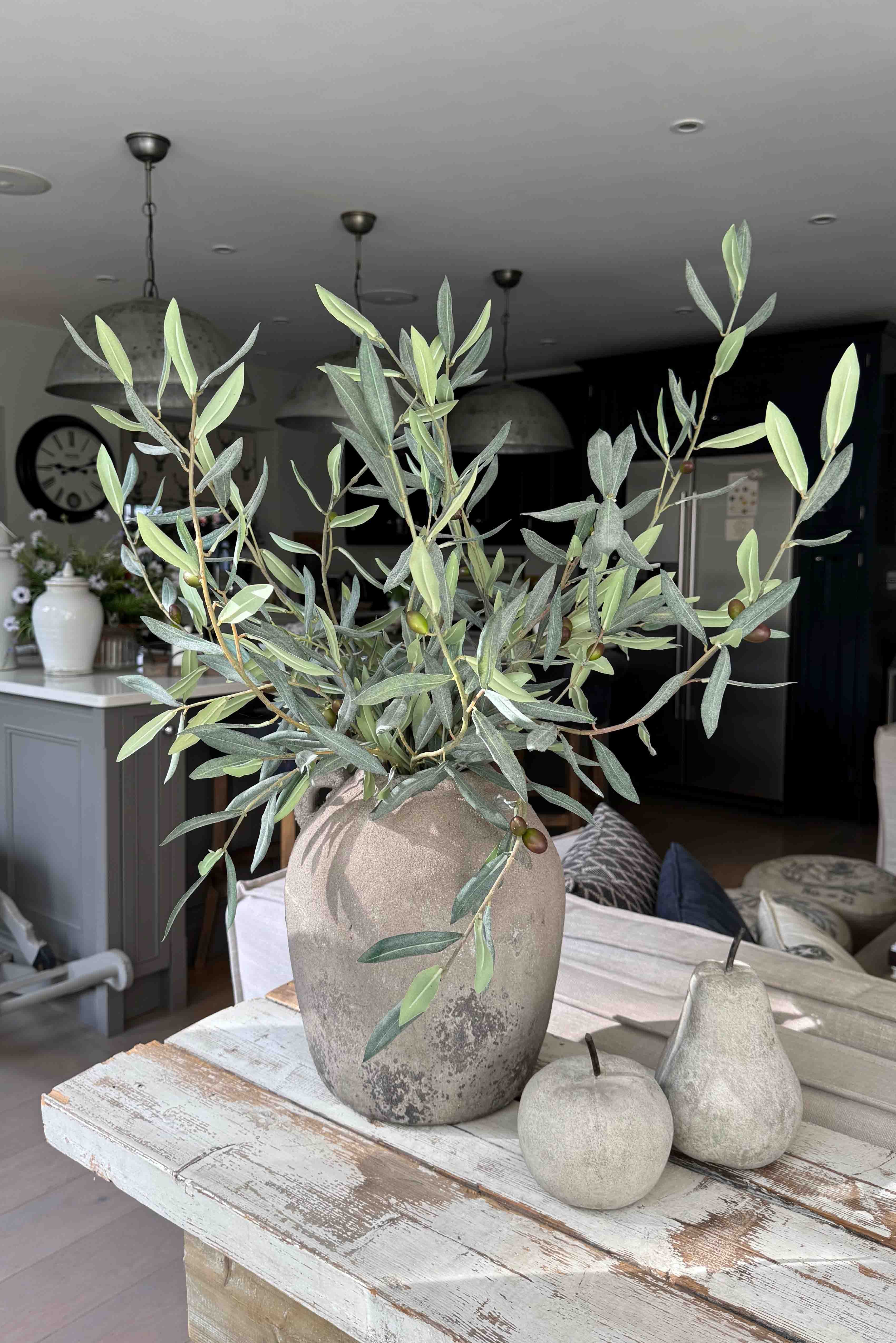 Potted artificial olive tree plant on a wooden table with a blurred indoor background