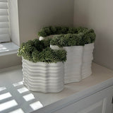 Three white textured planters with faux green plants on a white surface. Rtfact