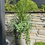 Artificial potted plant on a stone patio with a stone wall and garden in the background. 