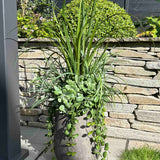 Artificial potted plant on a stone patio with a stone wall and garden in the background. 