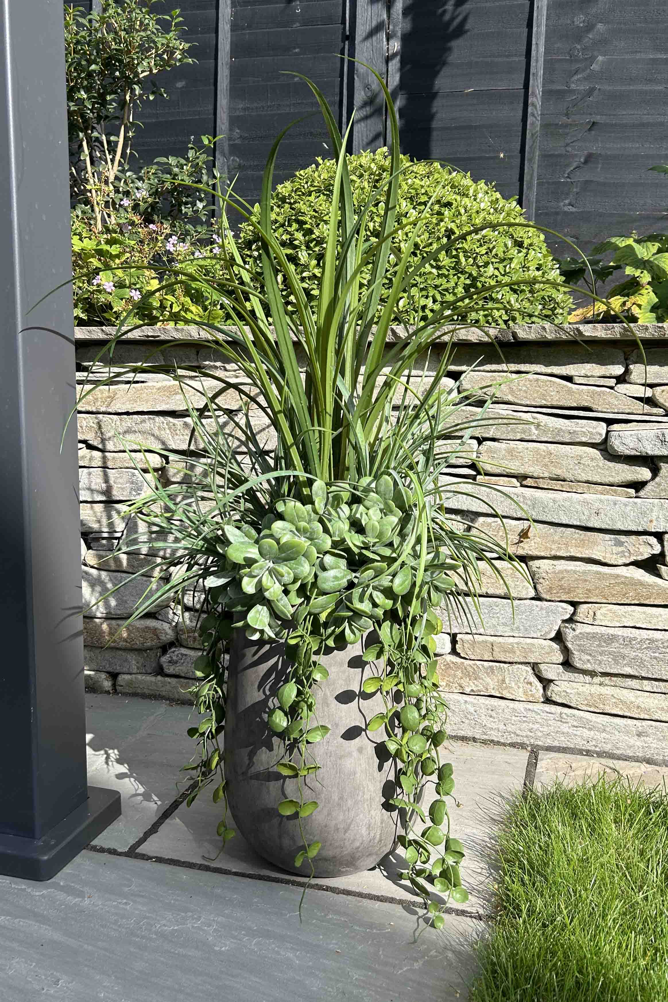 Artificial potted plant on a stone patio with a stone wall and garden in the background. 