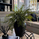 Decorative vase of faux greenery, diffuser, and books on a table. RTfact