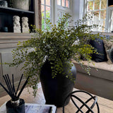 Decorative vase of faux greenery, diffuser, and books on a table. RTfact