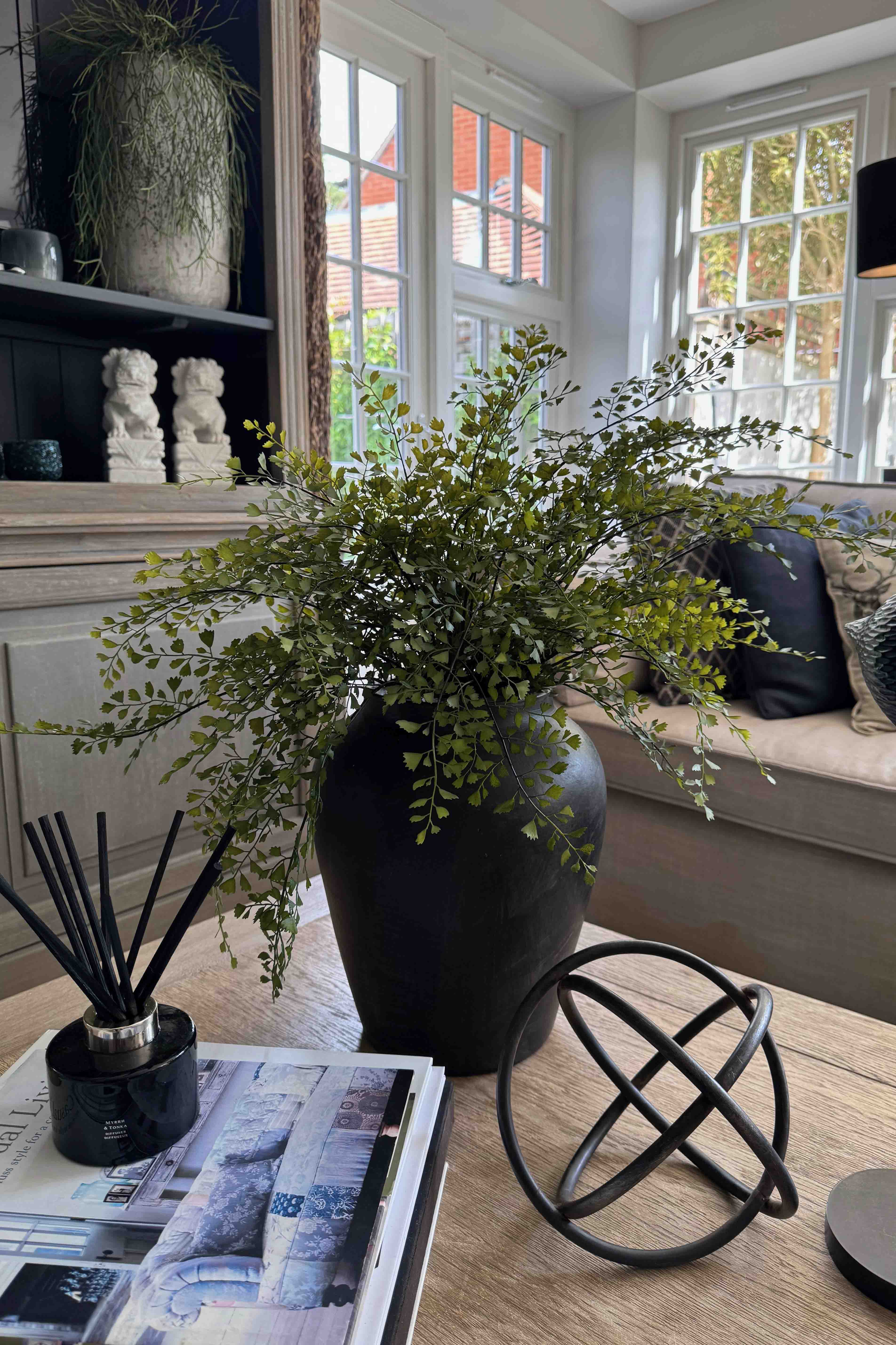 Decorative vase of faux greenery, diffuser, and books on a table. RTfact
