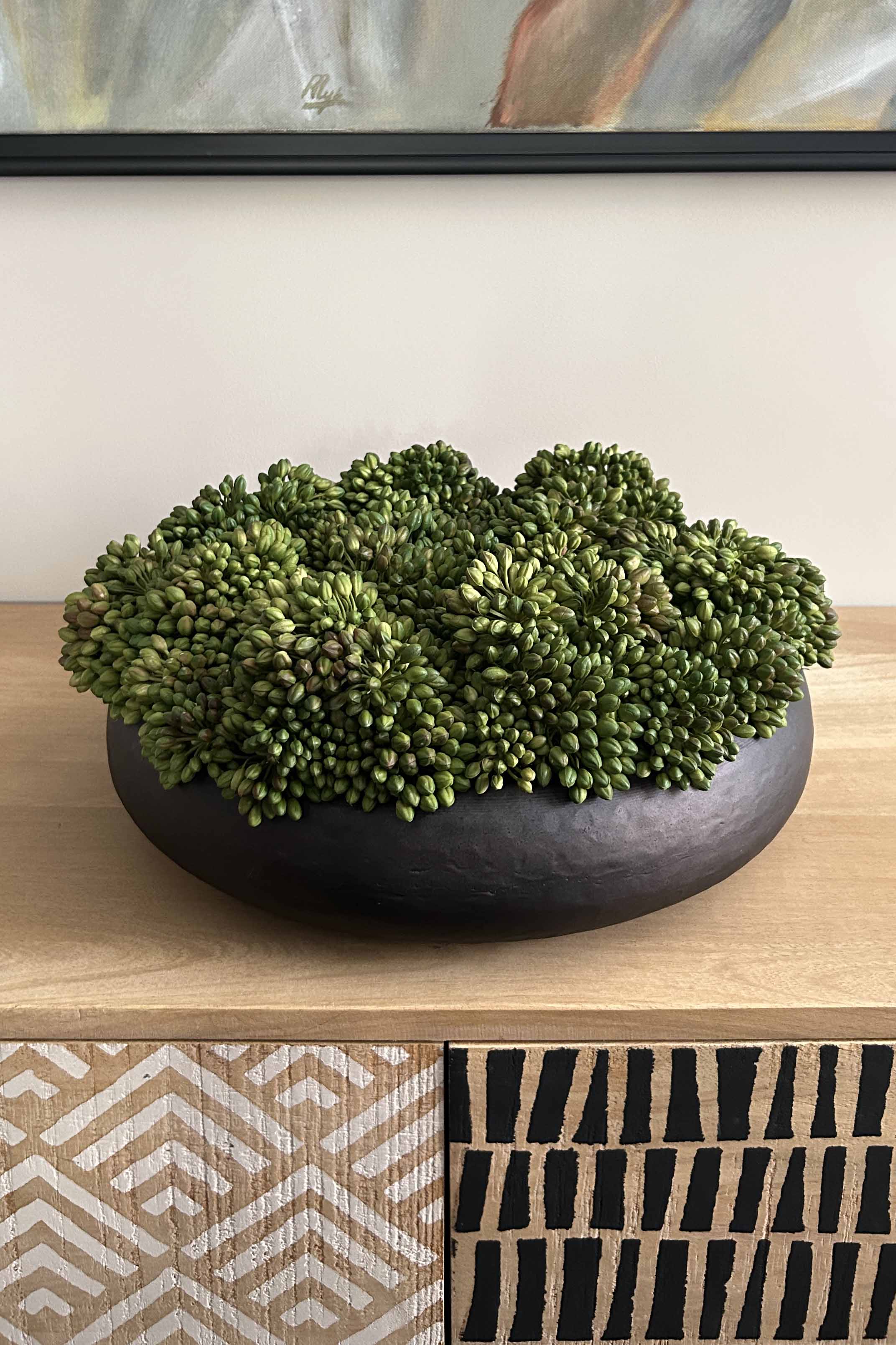 Green decorative ball in a black bowl on a wooden surface with a patterned wall in the background