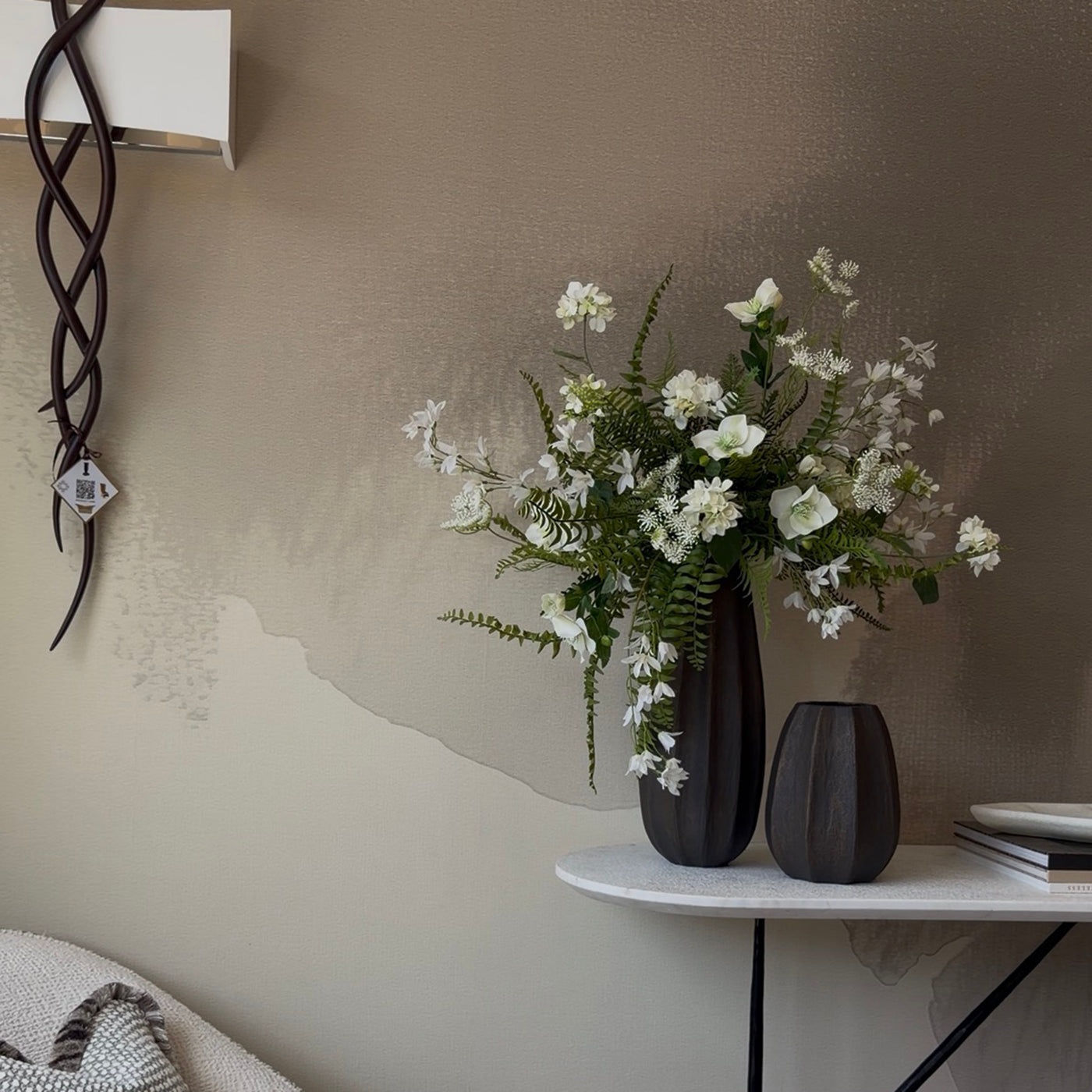 Floral arrangement in a black vase on a white table against a beige wall.