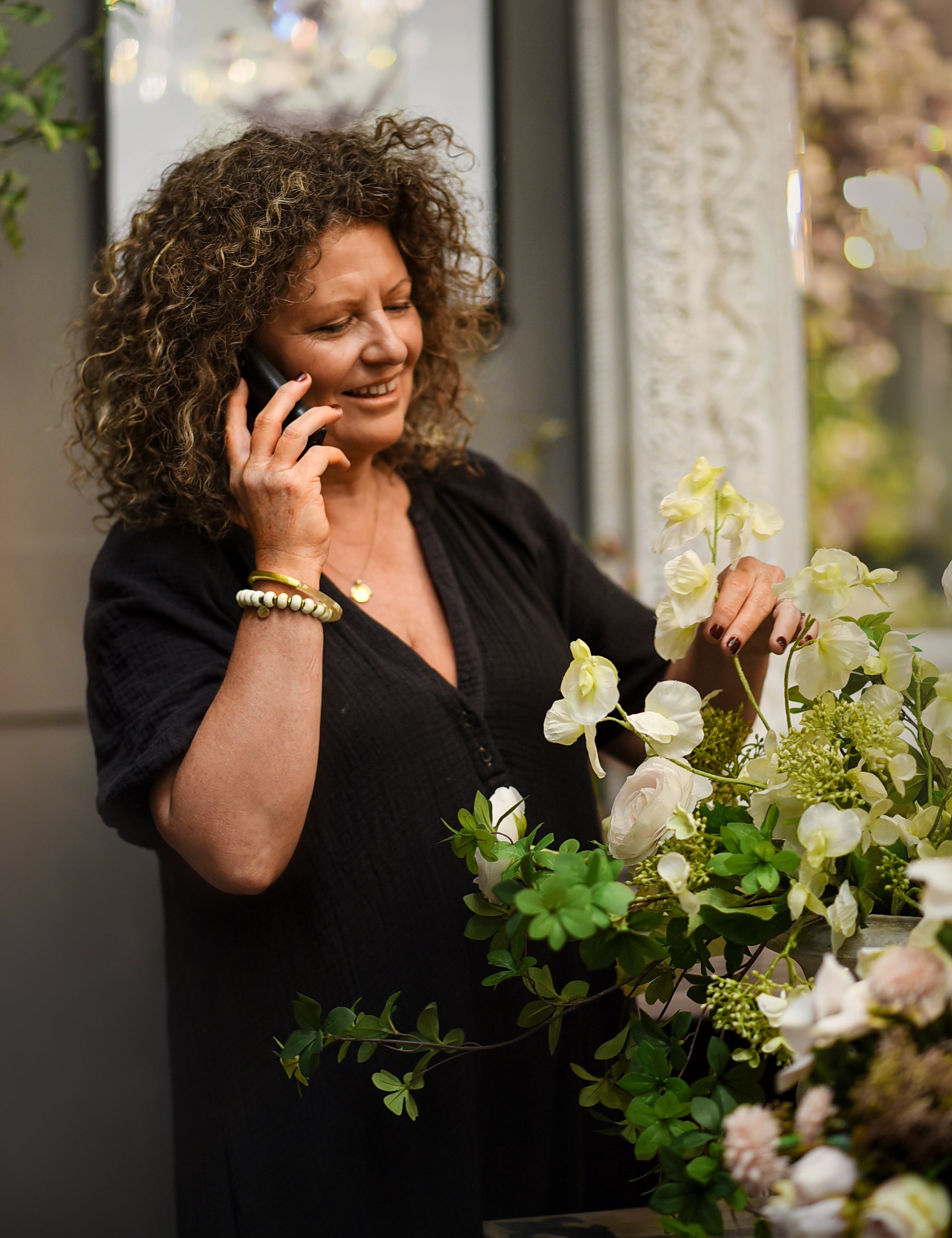 Woman talking on a phone next to a floral arrangement indoors