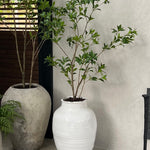 Artificial tree in a white vase with green plant against a neutral wall