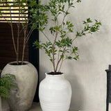 Artificial tree in a white vase with green plant against a neutral wall