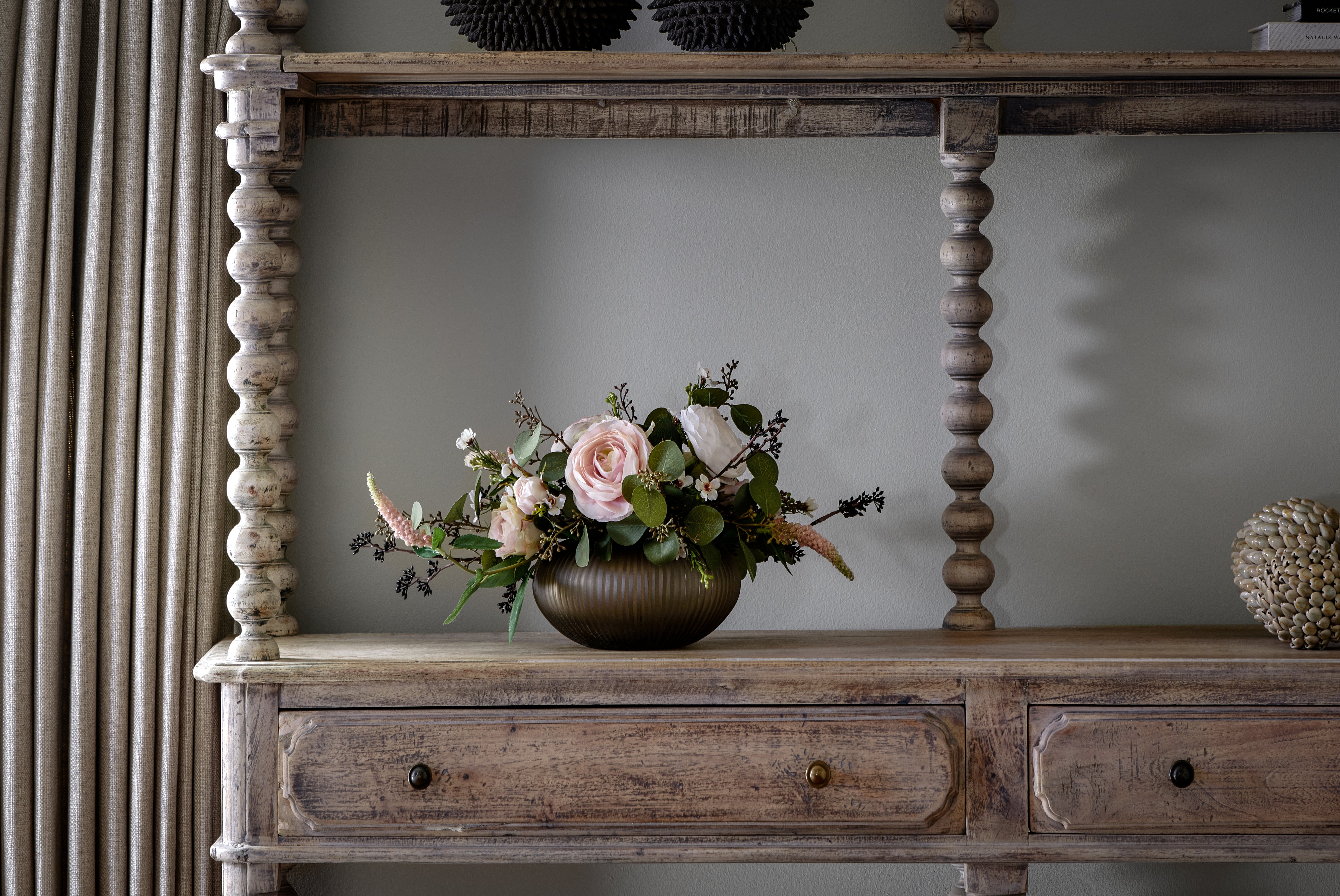 Floral arrangement in a pot on a wooden console table against a gray wall.